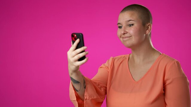 Copy space portrait of happy smiling gender fluid non binary young woman 20s using speaking talking on mobile cell phone conducting pleasant conversation isolated on pink background studio. 