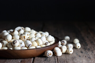 Dried lotus seeds in a wooden tray on a rustic wooden floor, selective focus.