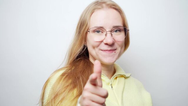Young beautiful blonde woman in glasses and casual yellow sweater turns around, wave her hair, point at the camera with her finger, and express that you are good. White studio background stock video