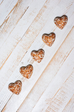 Sweet heart-shaped glazed gingerbread photographed on a white wooden surface.