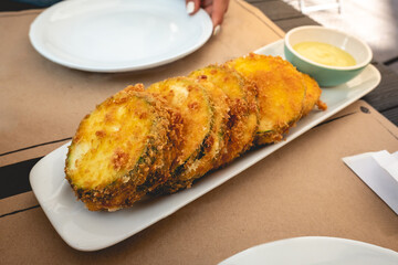 Delicious vegan fried pumpkin in panko with avocado sauce in white plates in a table and girl with white nails at vegan restaurant 