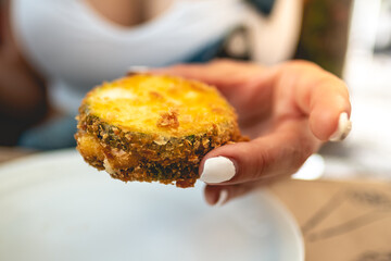 Hand of girl with white nails holding a vegan fried pumpkin in panko over white plates in a table at vegan restaurant
