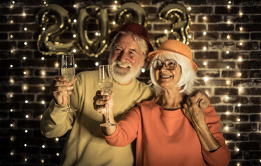 Fototapeta na wymiar Blurred cheerful senior couple holding champagne flutes having party by night. Happiness lifestyle for mature retired people waiting for new year 2023