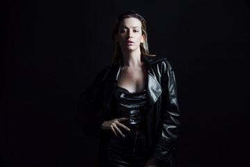 Stylish portrait of a young beautiful woman in a black leather raincoat on a black background. Trendy beautiful blonde