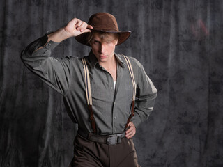 A young man in retro style, an adventure character. A guy in a hat and a gray shirt, breeches with...