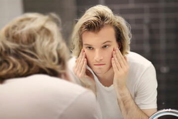 young man looking in the mirror,combing his hair,looking at problems on face.