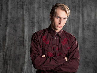 an attractive man in an elegant suit, burgundy shirt with embroidery. Photo in the studio on a gray background
