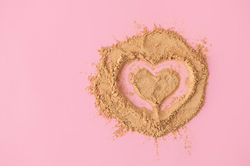 Top view of heart shape made of raw maca root powder on soft pink background with copy space