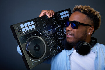 Cool guy in dark glasses walks into club and holds DJ console on his shoulder. Dark skinned DJ in...