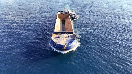 Aerial drone photo of assisted with tug boat empty barge boat cruising in deep blue sea