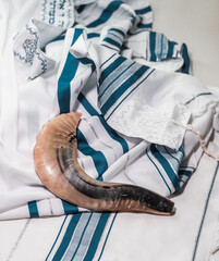 Shofar, the animal horn blown on Yom Kippur, lies on a blue and white tallit. Jewish religious...