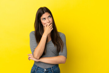 Young Brazilian woman isolated on yellow background having doubts and with confuse face expression