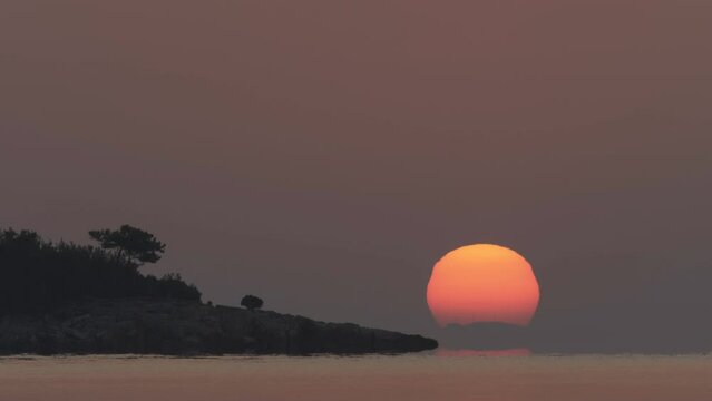 Timelapse of sunrise from the sea near the coast with a pine tree silhouette, Thassos Island in Greece