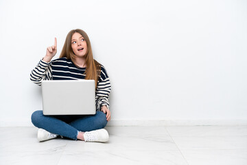 Young caucasian woman with a laptop sitting on the floor isolated on white background intending to realizes the solution while lifting a finger up