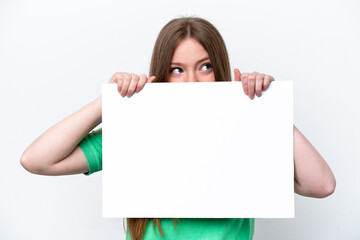 Young caucasian woman isolated on white background holding an empty placard and hiding behind it