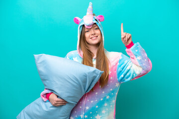 Young caucasian girl with unicorn pajamas holding pillow isolated on blue background pointing up a great idea
