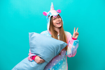 Young caucasian girl with unicorn pajamas holding pillow isolated on blue background smiling and...