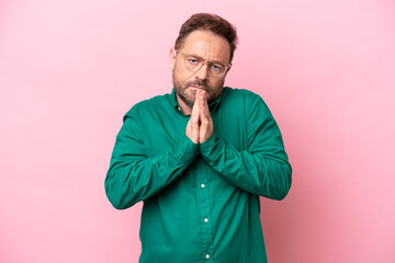 Middle age caucasian man isolated on pink background keeps palm together. Person asks for something