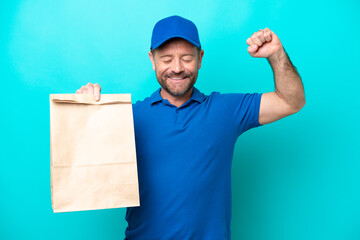 Middle age man taking a bag of takeaway food isolated on blue background doing strong gesture