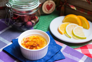 Portion of dessert crème brûlée with caramel crust in ramekin with orange slices on a plate