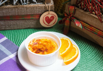 Portion of dessert crème brûlée with caramel crust in ramekin with orange slices on a plate