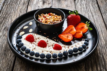 Yogurt with strawberries, blueberries, raspberries and muesli in bowl on wooden table
