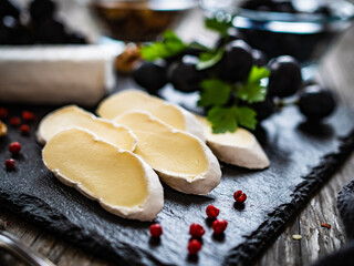 Camembert cheese with grapes and walnuts on stony cutting board on wooden table
