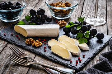 Camembert cheese with grapes and walnuts on stony cutting board on wooden table
