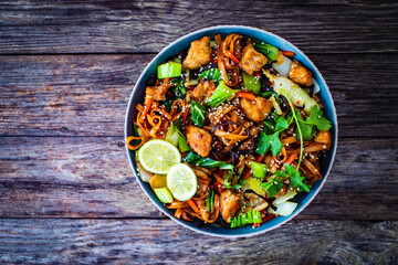 Asian food - chicken nuggets, noodles, stir fried vegetables, soy sauce and mushrooms on wooden table
