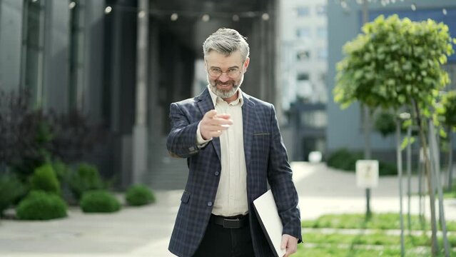 Smiling mature professor teacher looking at camera and showing inviting gesture with hands ask to join study in modern educational building Admission to university and introductory campaign concept 