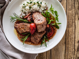 Roast pork loin with plums in sauce and white rice on wooden table
