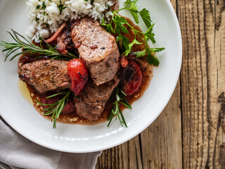 Roast pork loin with plums in sauce and white rice on wooden table
