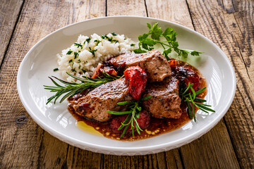 Roast pork loin with plums in sauce and white rice on wooden table
