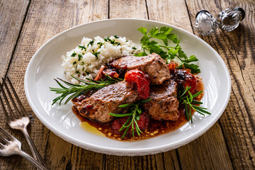 Roast pork loin with plums in sauce and white rice on wooden table
