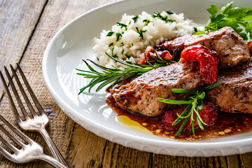 Roast pork loin with plums in sauce and white rice on wooden table
