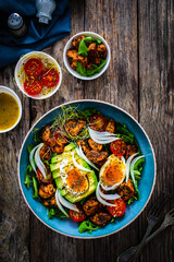 Tasty salad - fried chicken breast, avocado, boiled eggs, mini tomatoes and fresh green vegetables on wooden background
