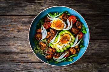 Tasty salad - fried chicken breast, avocado, boiled eggs, mini tomatoes and fresh green vegetables on wooden background
