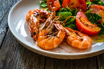 Fried prawns in garlic sauce with greens and tomatoes on wooden table