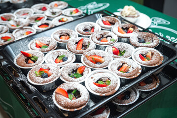 Many servings of chocolate fondant with strawberries and blueberries, sprinkled with powdered sugar