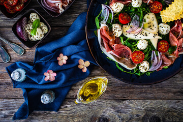 Obraz na płótnie Canvas Fresh salad - prosciutto di Parma, mozzarella, pear and leafy vegetables on wooden table 