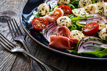 Fresh salad - prosciutto di Parma, mozzarella, pear and leafy vegetables on wooden table
