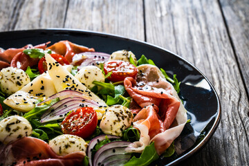 Fresh salad - prosciutto di Parma, mozzarella, pear and leafy vegetables on wooden table

