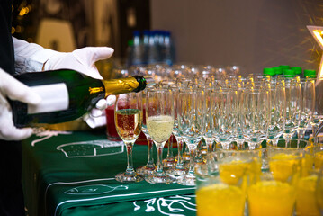 The waiter pours champagne into glasses. The waiter's hands are in white gloves.