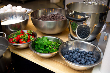 Ingredients for the dessert in bowls on the table. Chocolate drops, flour, strawberries, fresh mint leaves, blueberries.
