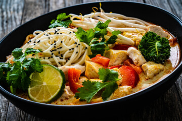 Tom Kha - Thai soup with chicken breast nuggets and noodles on wooden table

