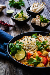 Tom Kha - Thai soup with chicken breast nuggets and noodles on wooden table
