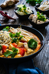 Tom Kha - Thai soup with chicken breast nuggets and noodles on wooden table
