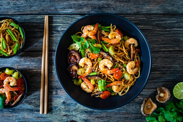 Mie noodles with fried prawns, shiitake mushrooms, coriander, carrot and celery on wooden table
