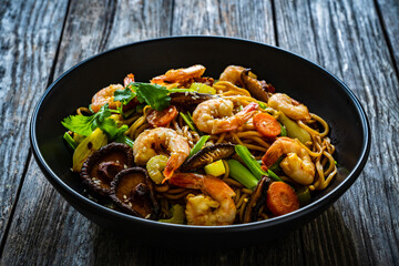 Mie noodles with fried prawns, shiitake mushrooms, coriander, carrot and celery on wooden table
