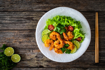 Fried panko prawns with lime, tomatoes and greens wooden table

